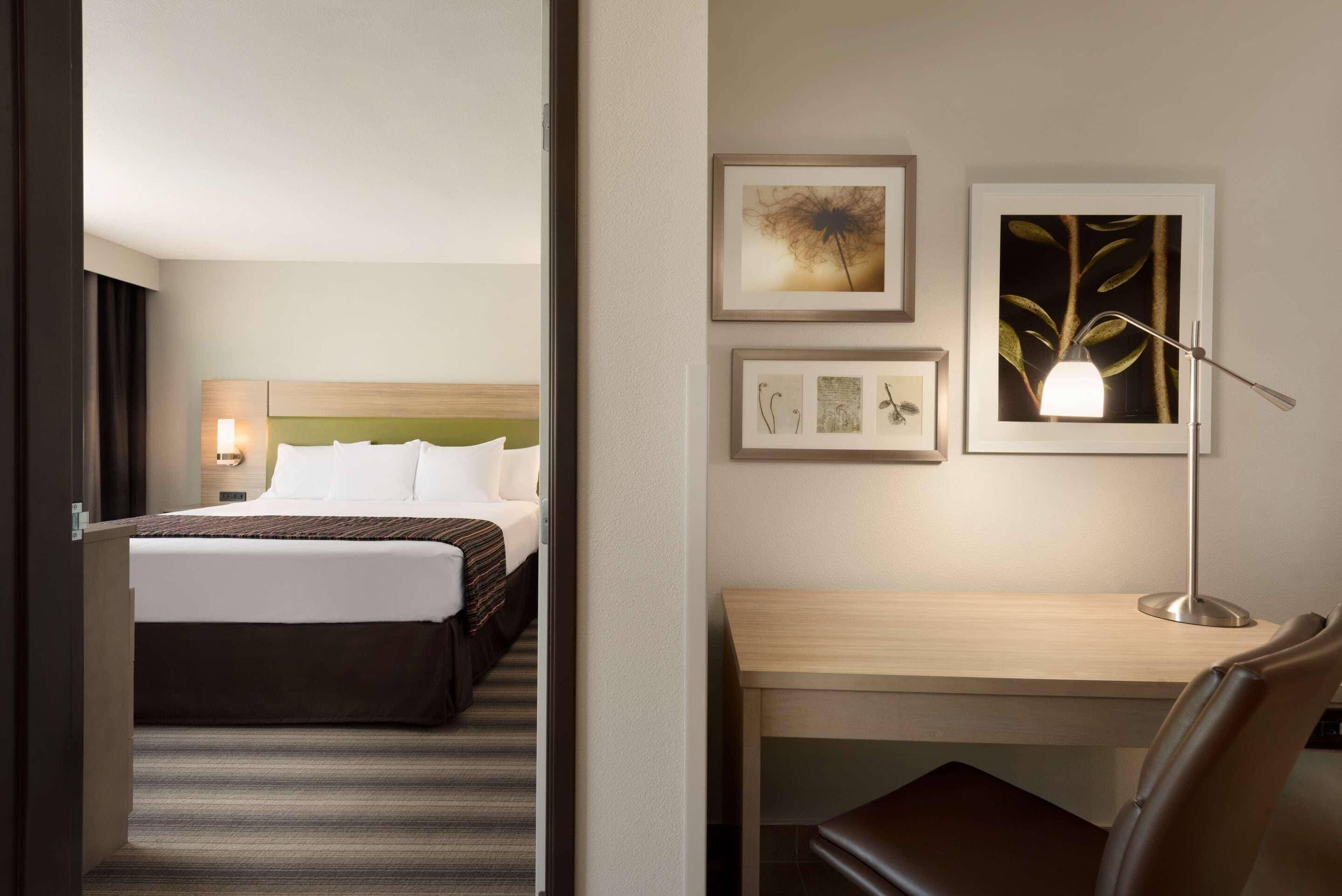 Quarto de hotel com cama, escrivaninha e cadeira. Quadros emoldurados na parede.