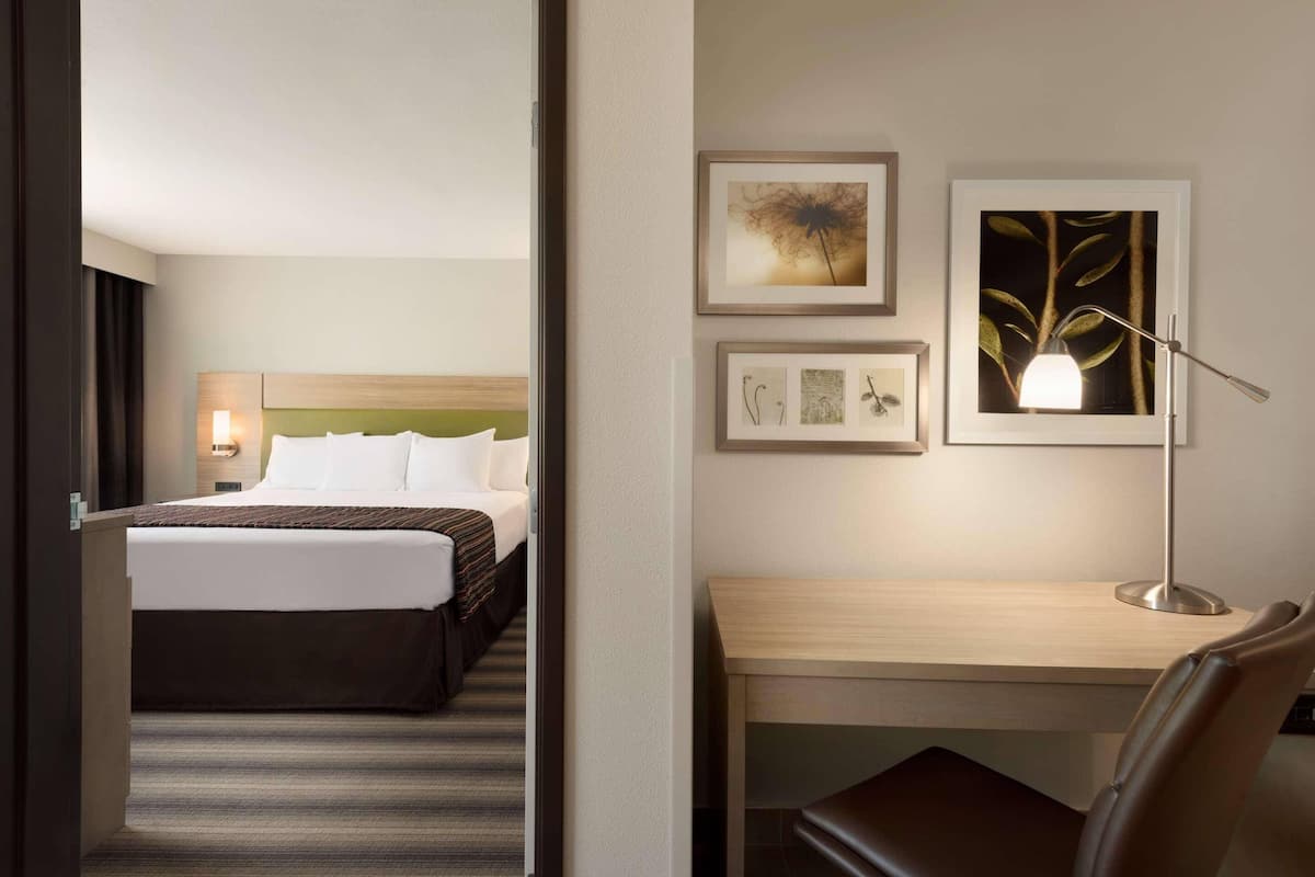 Quarto de hotel com cama, escrivaninha e cadeira. Quadros emoldurados na parede.