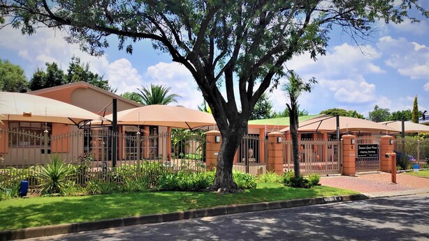 A hotel with a large tree in front, a gated entrance, and a well-maintained lawn. - Premiere Guest House (Bloemfontein)