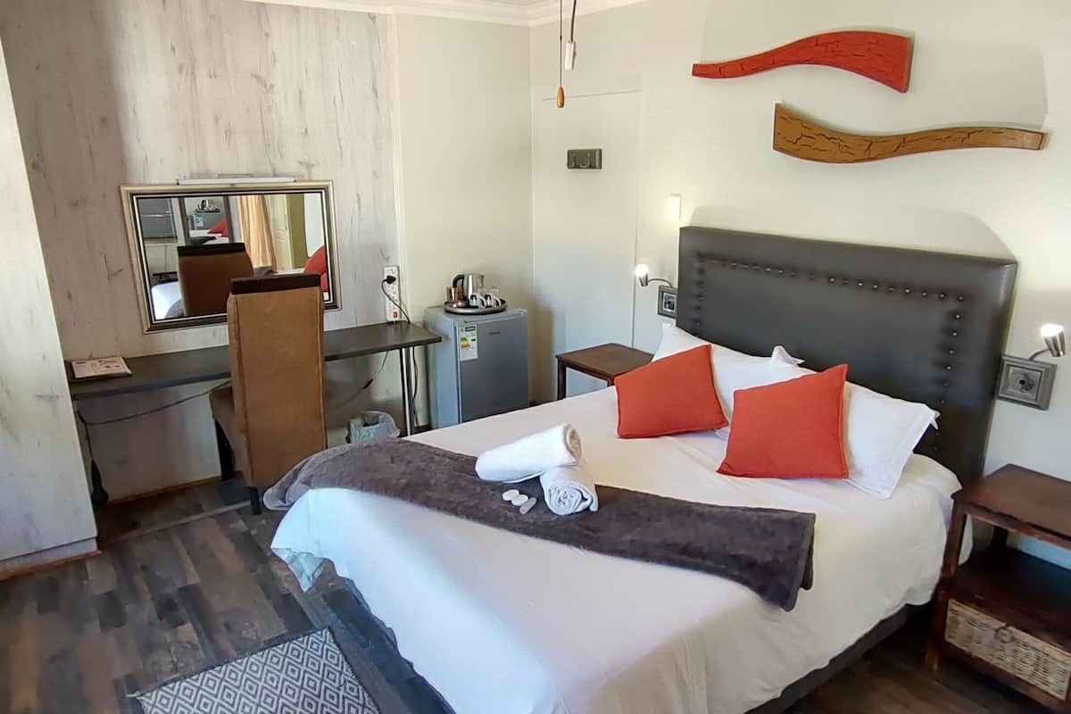 Ein Hotelzimmer mit Bett, Nachttisch, Schminktisch, Kommode, Spiegel und Holzboden.