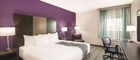 A hotel room with a large bed, two bedside tables with lamps, a desk with a chair, and a window with curtains.