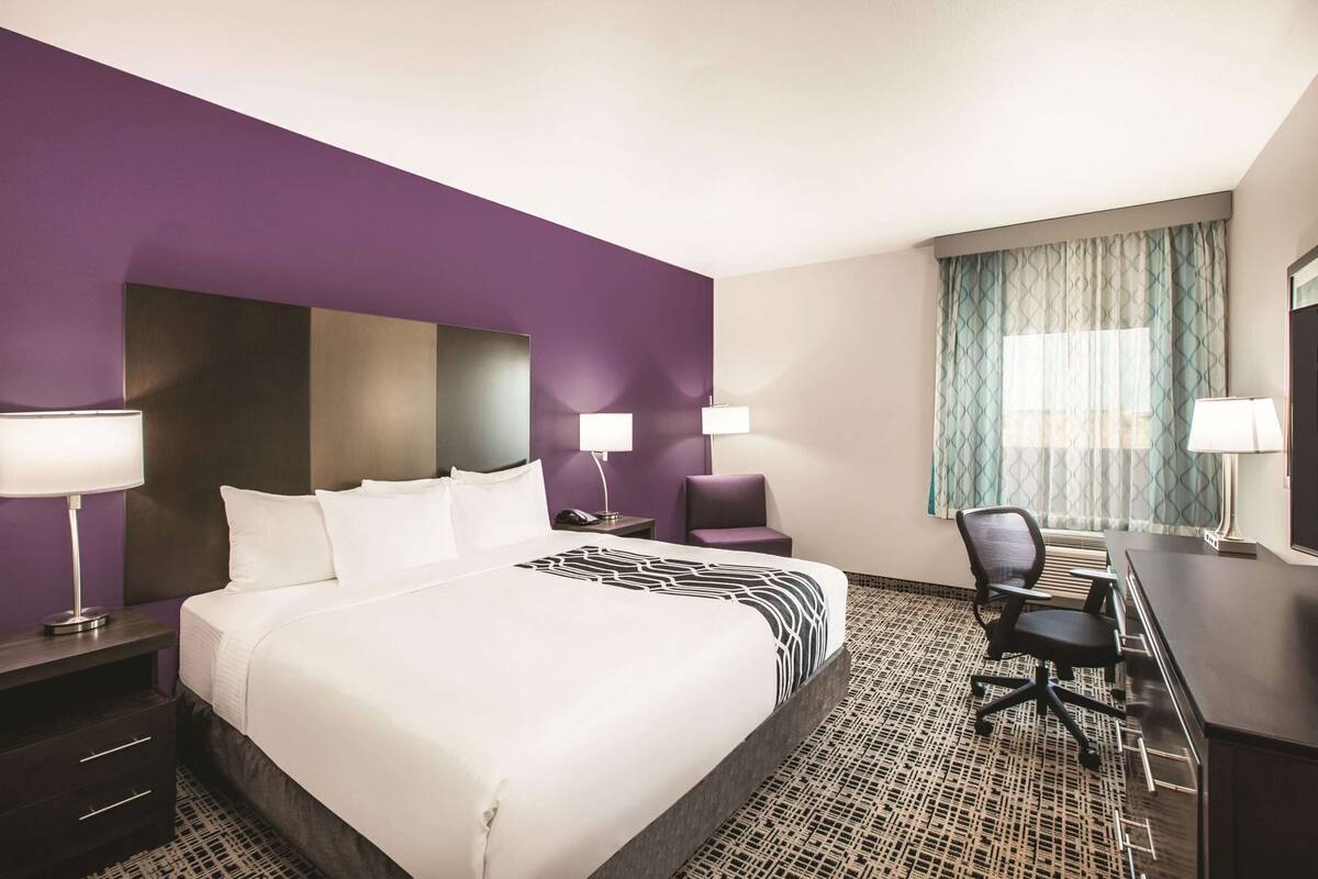 Een hotelkamer met een groot bed, twee nachtkastjes, een bureau, een stoel en een raam met gordijnen.