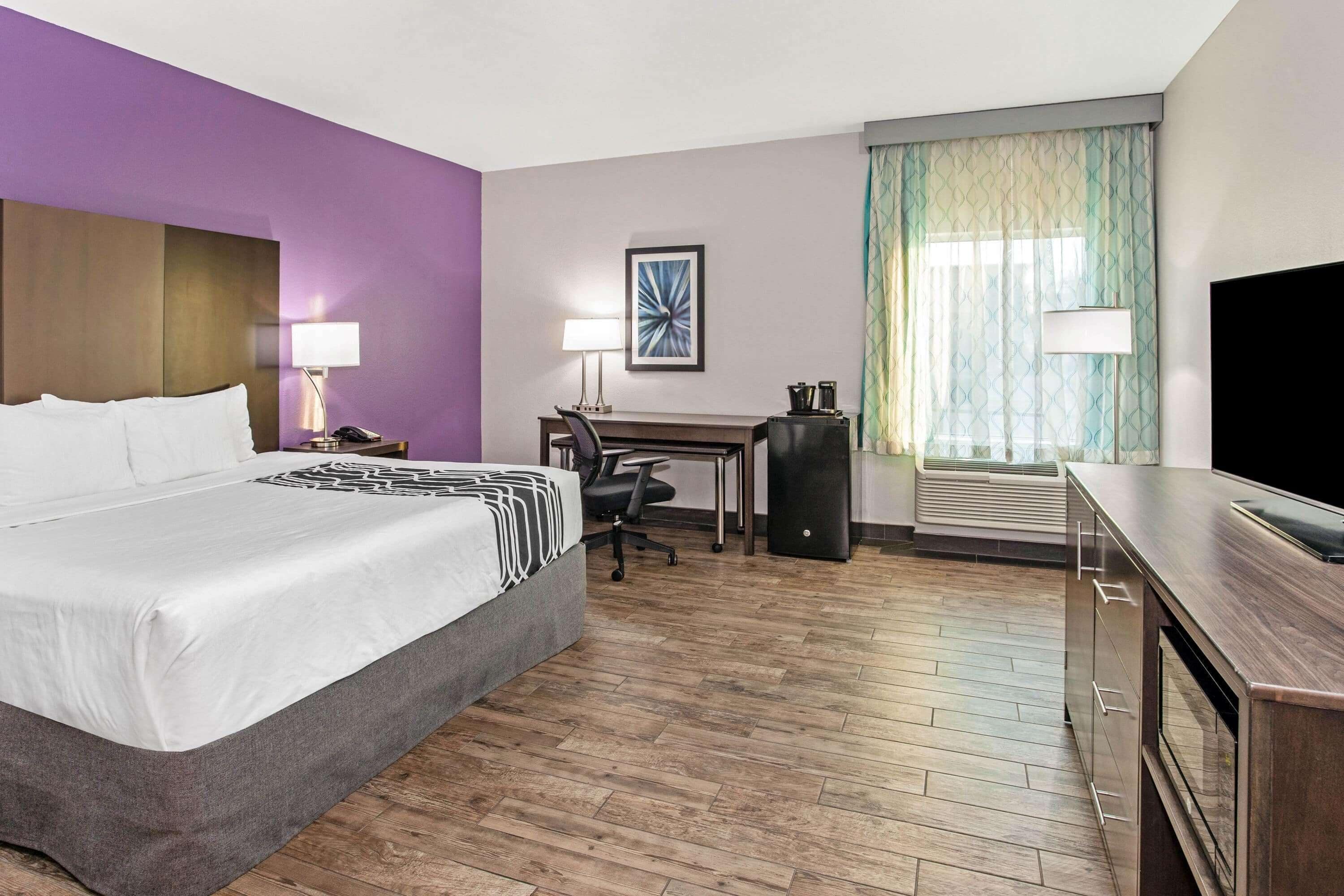 Habitación de hotel con una cama grande, un escritorio, una silla, un televisor y una ventana con cortinas.