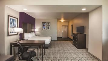 A hotel room with a bed, desk, chair, dresser, TV, and artwork on the walls.