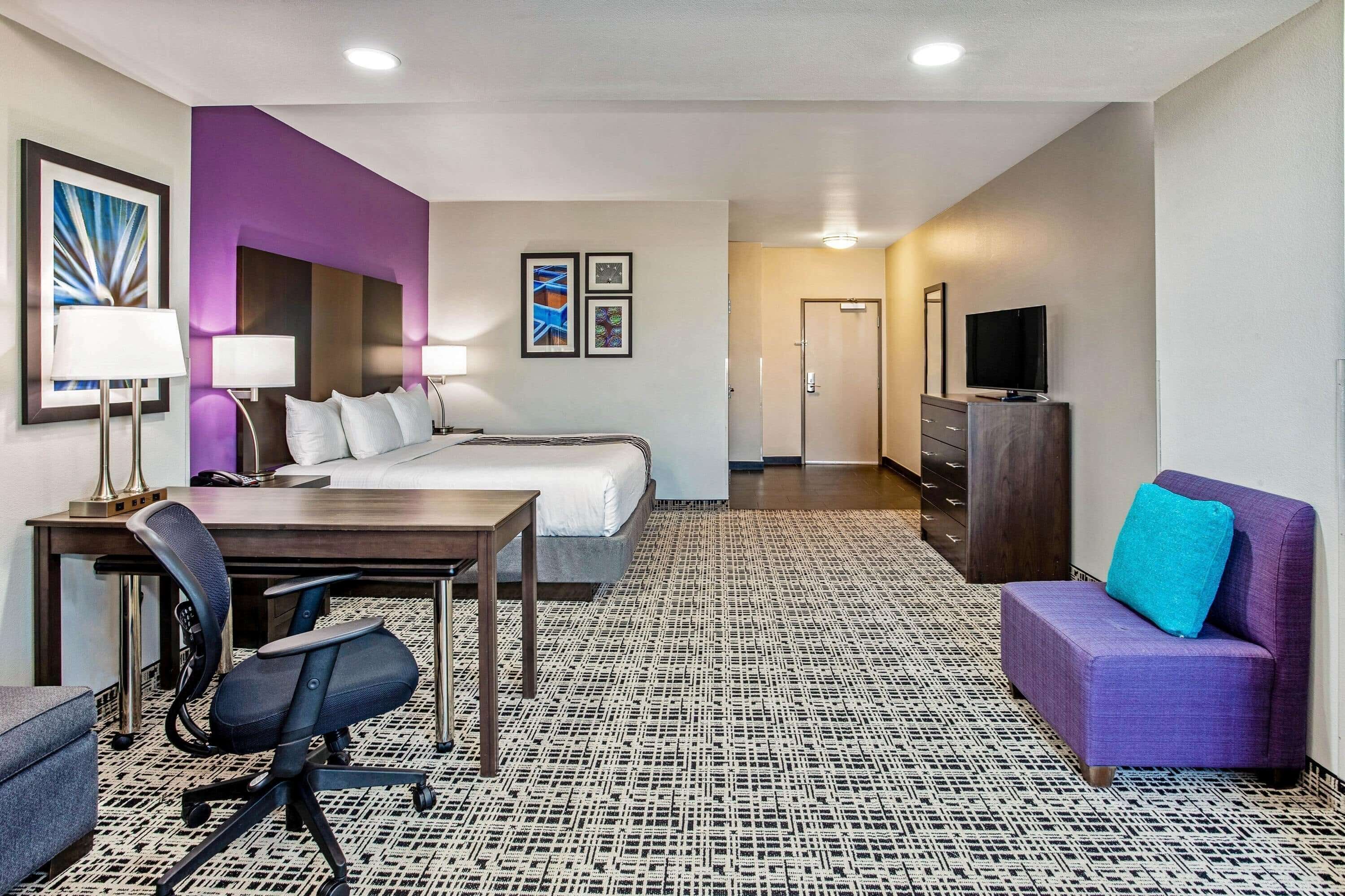 Une chambre d’hôtel avec un lit, un bureau, une chaise et un canapé violet.