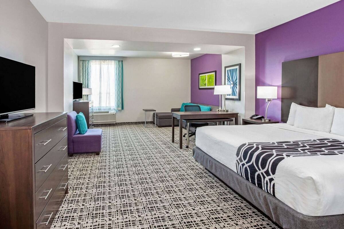 Een hotelkamer met een bed, een bureau, een stoel, een televisie en een badkamer die door een geopende deur zichtbaar is.