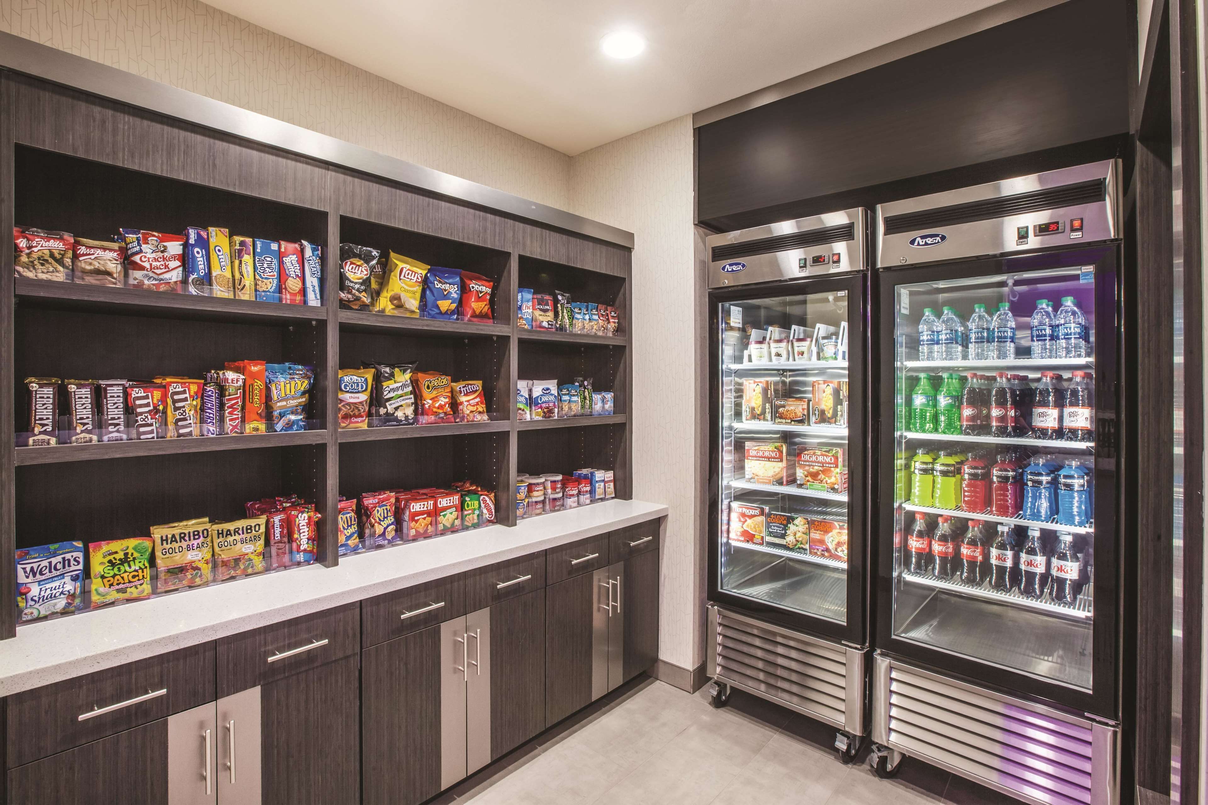 Un espacio con aperitivos y bebidas, con estantes llenos de diferentes opciones y dos refrigeradores para bebidas.