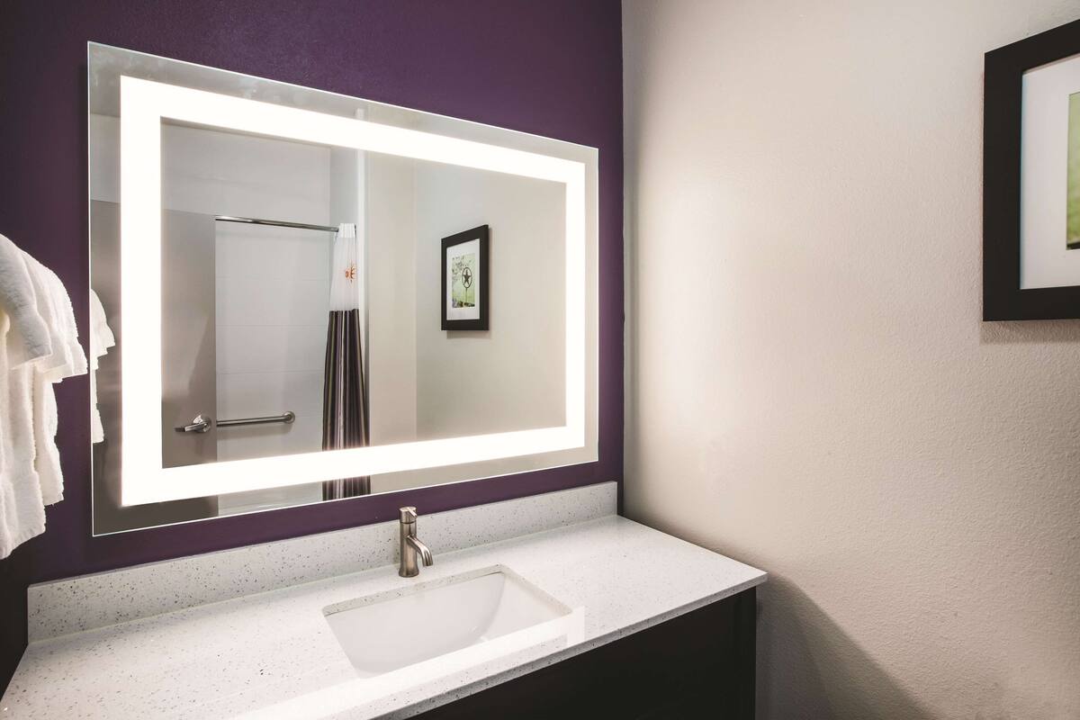 Een badkamer met een grote spiegel, een wit wastafelmeubel en een handdoekhouder.