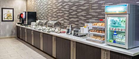 Uma mesa de pequeno-almoço com uma máquina de café, um frigorífico Liebherr e uma vitrine com pastelaria.