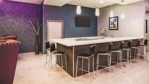 Een moderne barruimte met een lange toonbank, meerdere barstoelen, een flatscreen-tv en hanglampen.