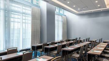 Une salle de conférence dotée de plusieurs tables et chaises, de grandes fenêtres avec des rideaux et d’un sol recouvert de moquette.