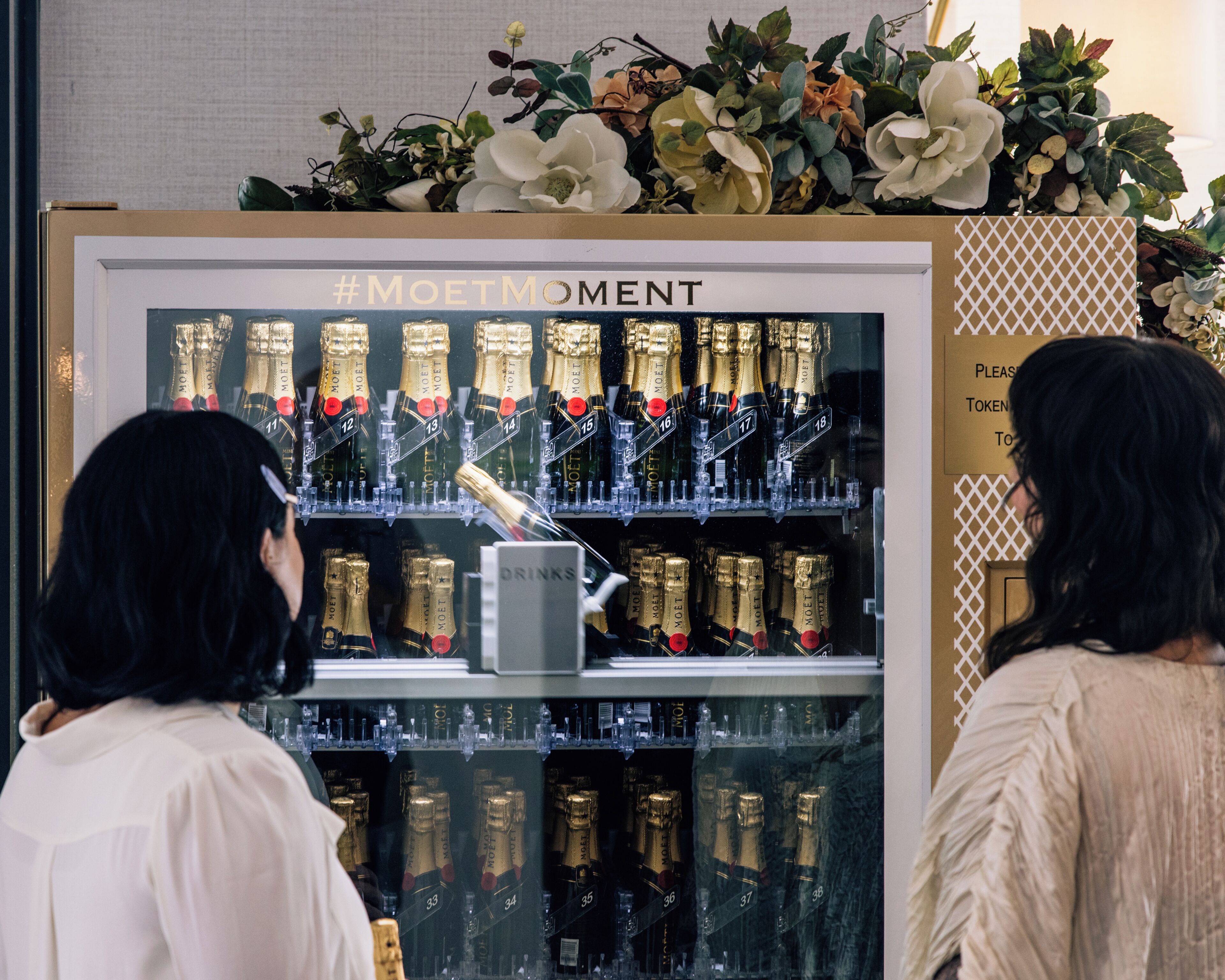 A display of champagne bottles with a sign reading 'DRINKS' and a hashtag '#MOETMOMENT'.