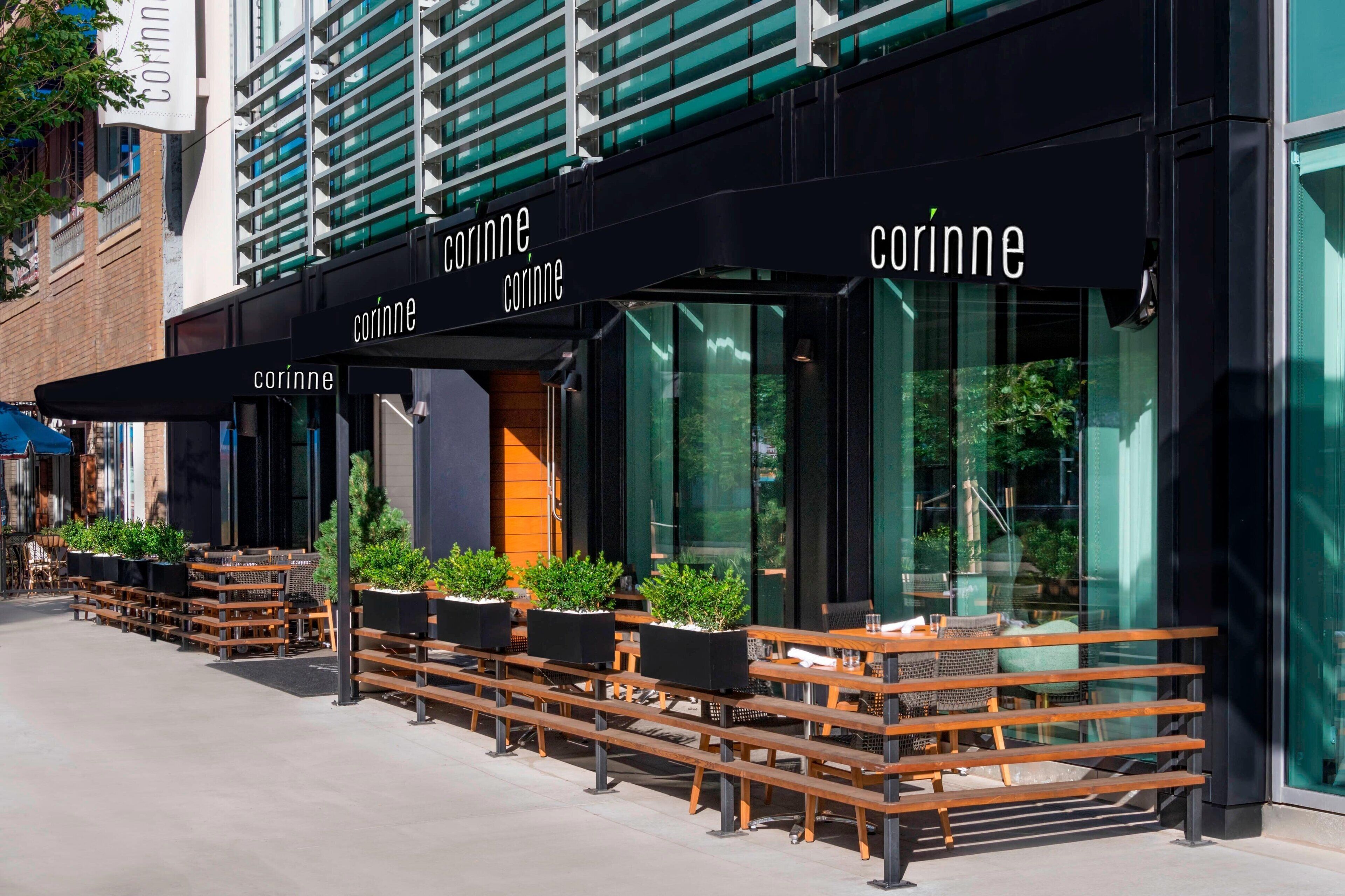 An outdoor seating area with wooden benches and tables, a black awning, and the name 'corinne' displayed above.