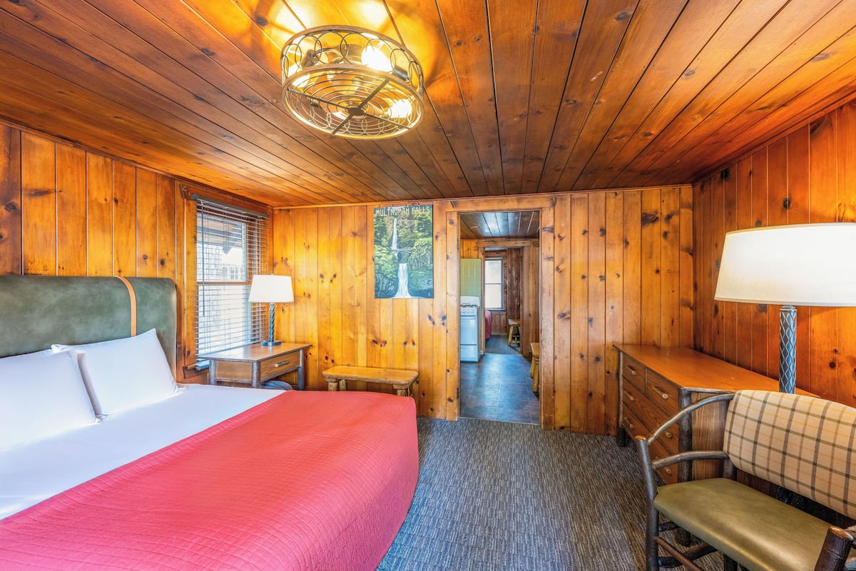 Quarto de cabana de madeira com cama, escrivaninha, cadeira e vista para uma floresta.
