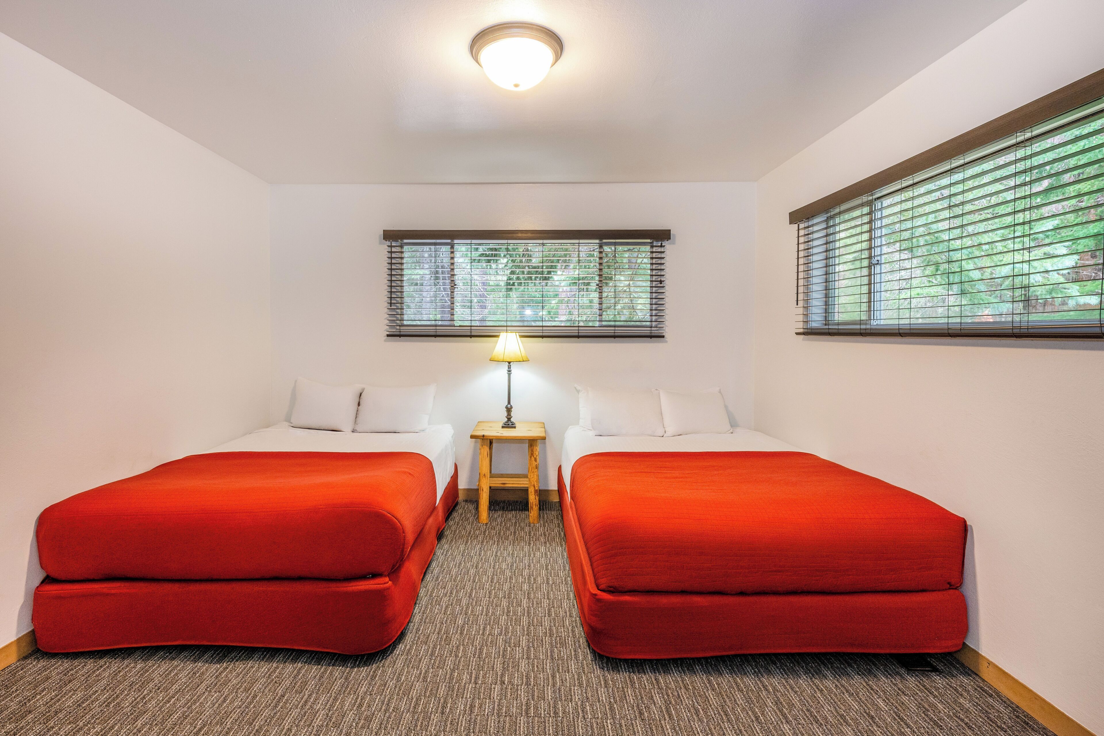 Ein Hotelzimmer mit zwei Einzelbetten, einem kleinen Tisch mit Lampe, einem Fenster mit Jalousien und einer Deckenleuchte.