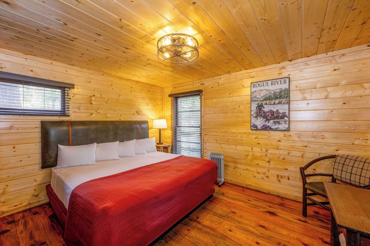 Quarto de cabana de madeira com uma cama, uma mesa e um cartaz na parede.
