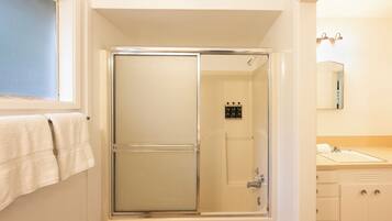Une salle de bain avec une douche en verre, une fenêtre avec une serviette et un lavabo avec un miroir.