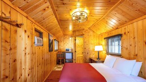 A wooden cabin room with a bed, a desk, a chair, a small TV, and a window with blinds. - Union Creek Resort (Prospect)