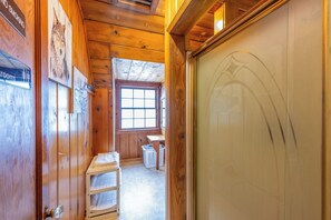 A wooden interior with a window, a door with a logo, a laundry basket, and a shelf with folded items.