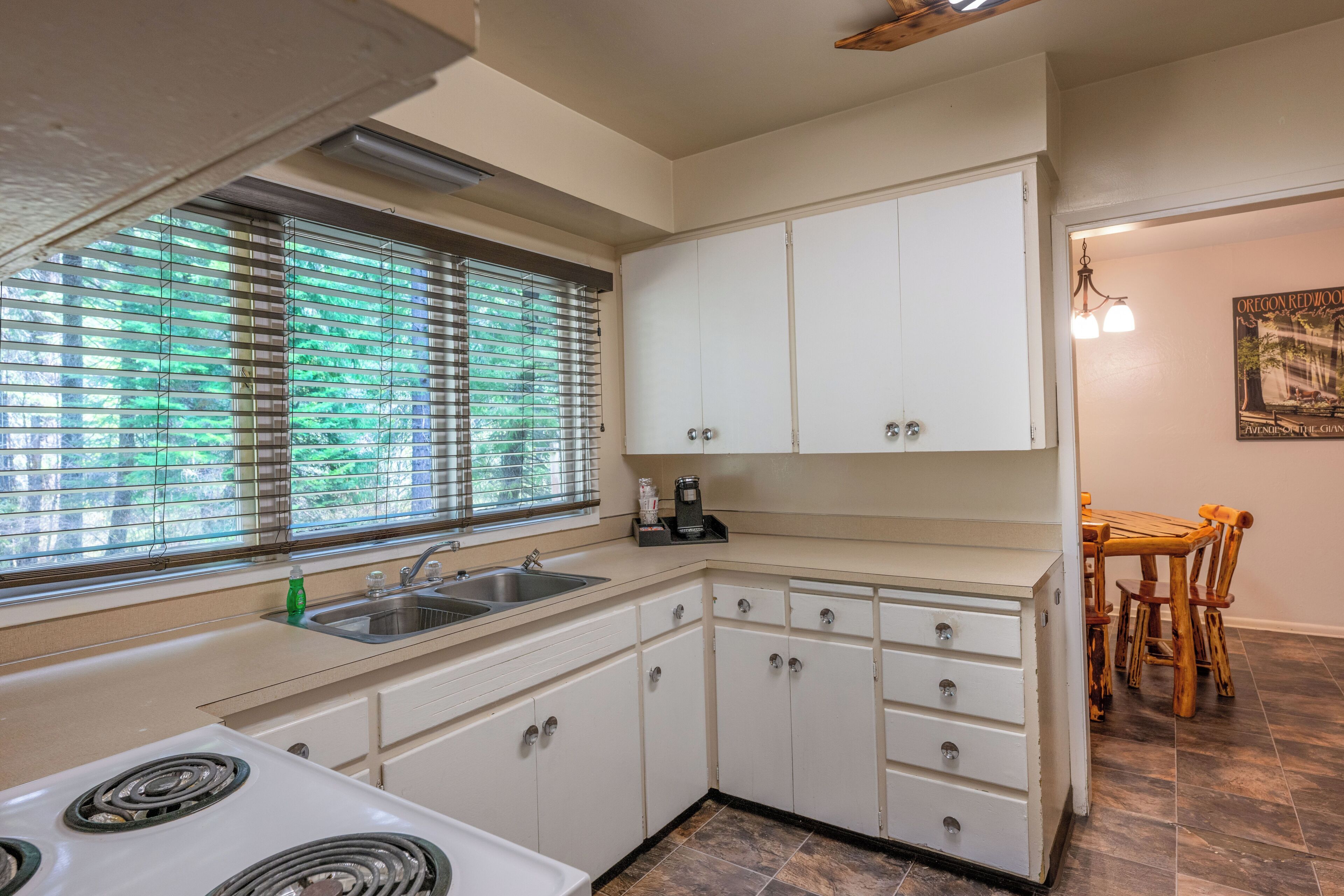 A kitchen with white cabinets, a stove, a sink, and a window with blinds.