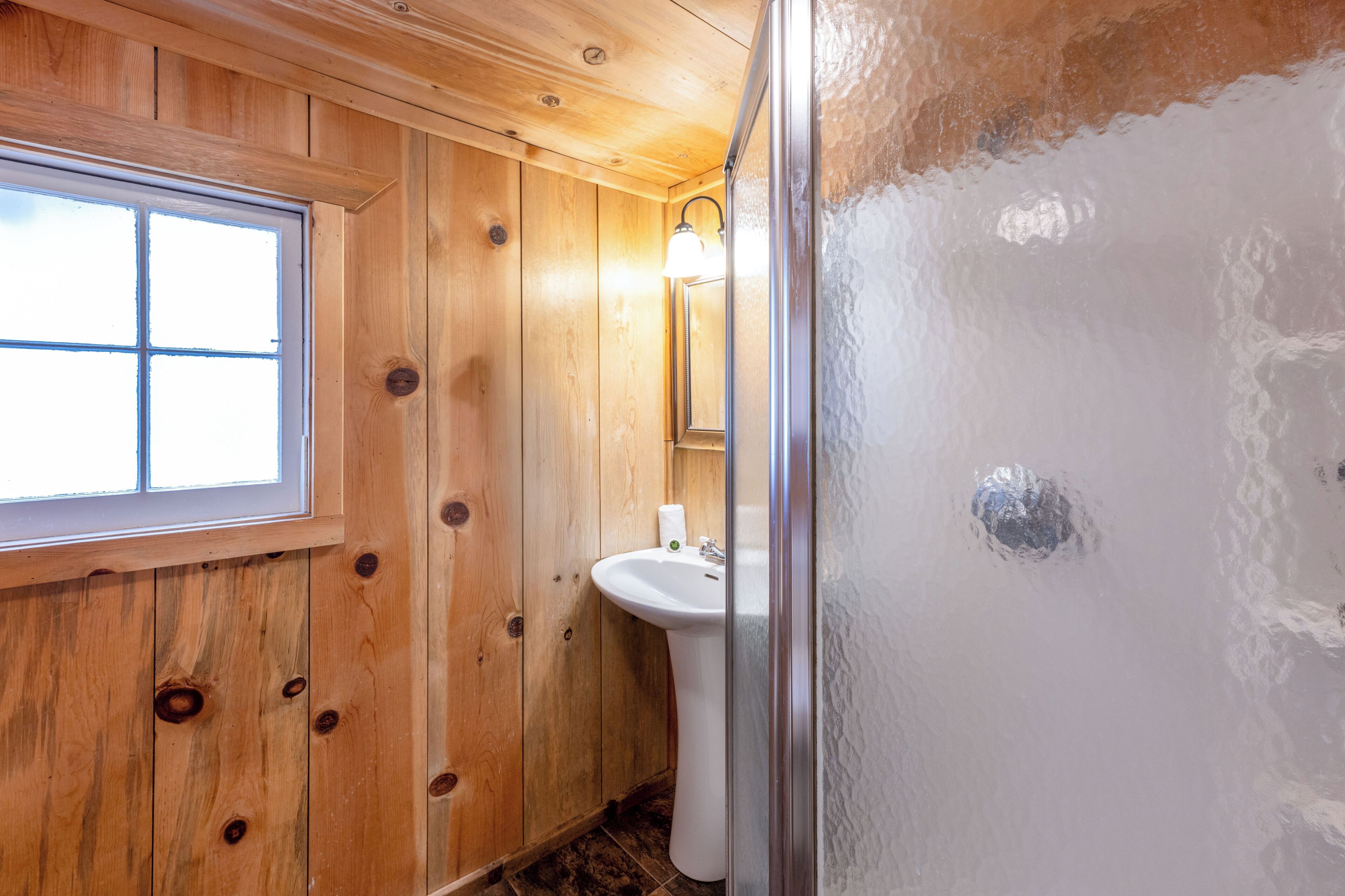 Une salle de bain aux murs lambrissés, avec une fenêtre, un lavabo et un miroir.