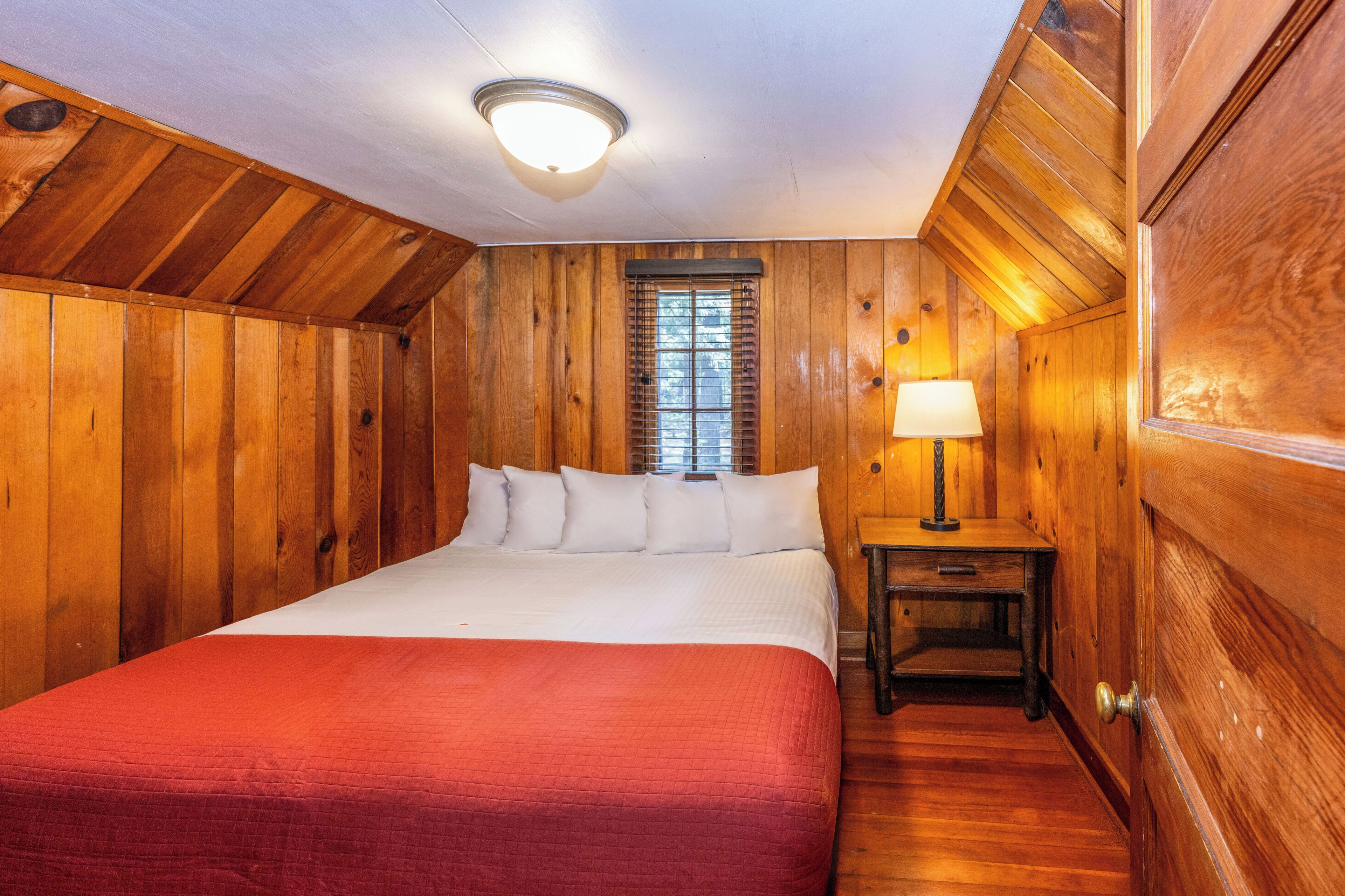 A wooden-paneled room with a bed, a nightstand, and a window.