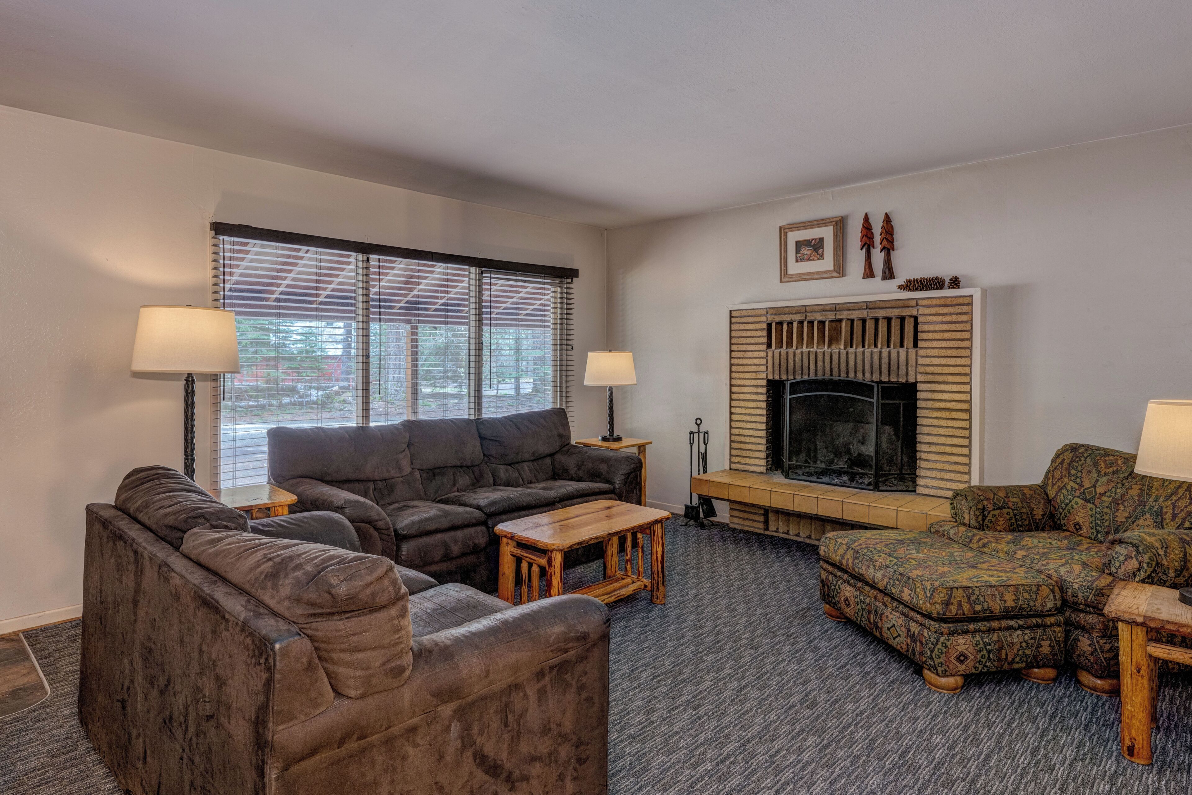 A living room with a fireplace, a sofa, a coffee table, and a patterned ottoman.