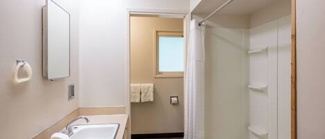 A bathroom with a sink, mirror, shower, and a towel rack.