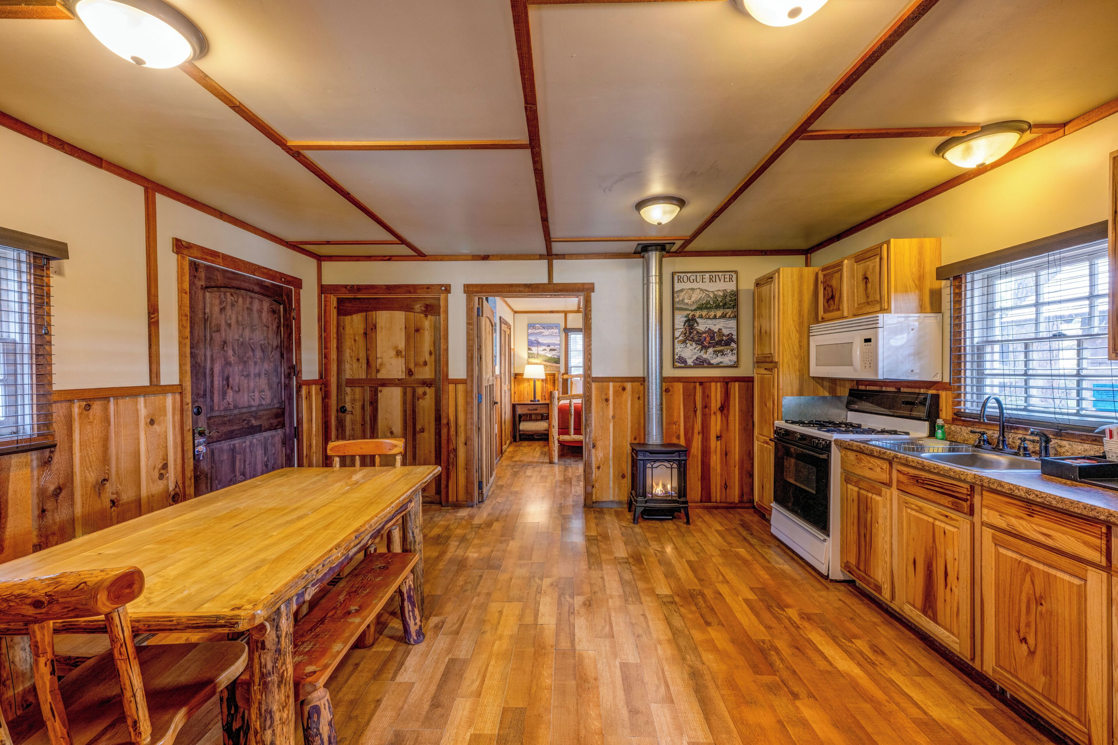 A wooden interior with a long dining table, wooden cabinets, a stove, and a refrigerator.