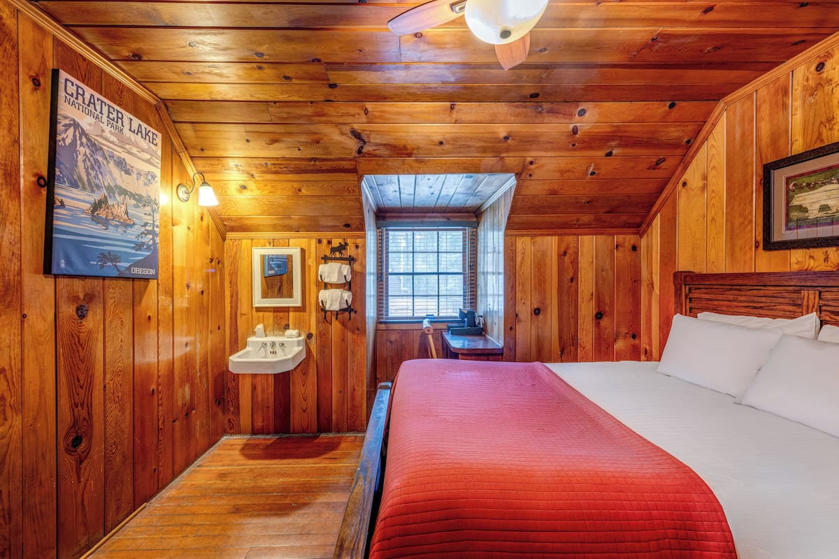 Quarto de cabana de madeira com uma cama, janela, pia e um cartaz na parede.