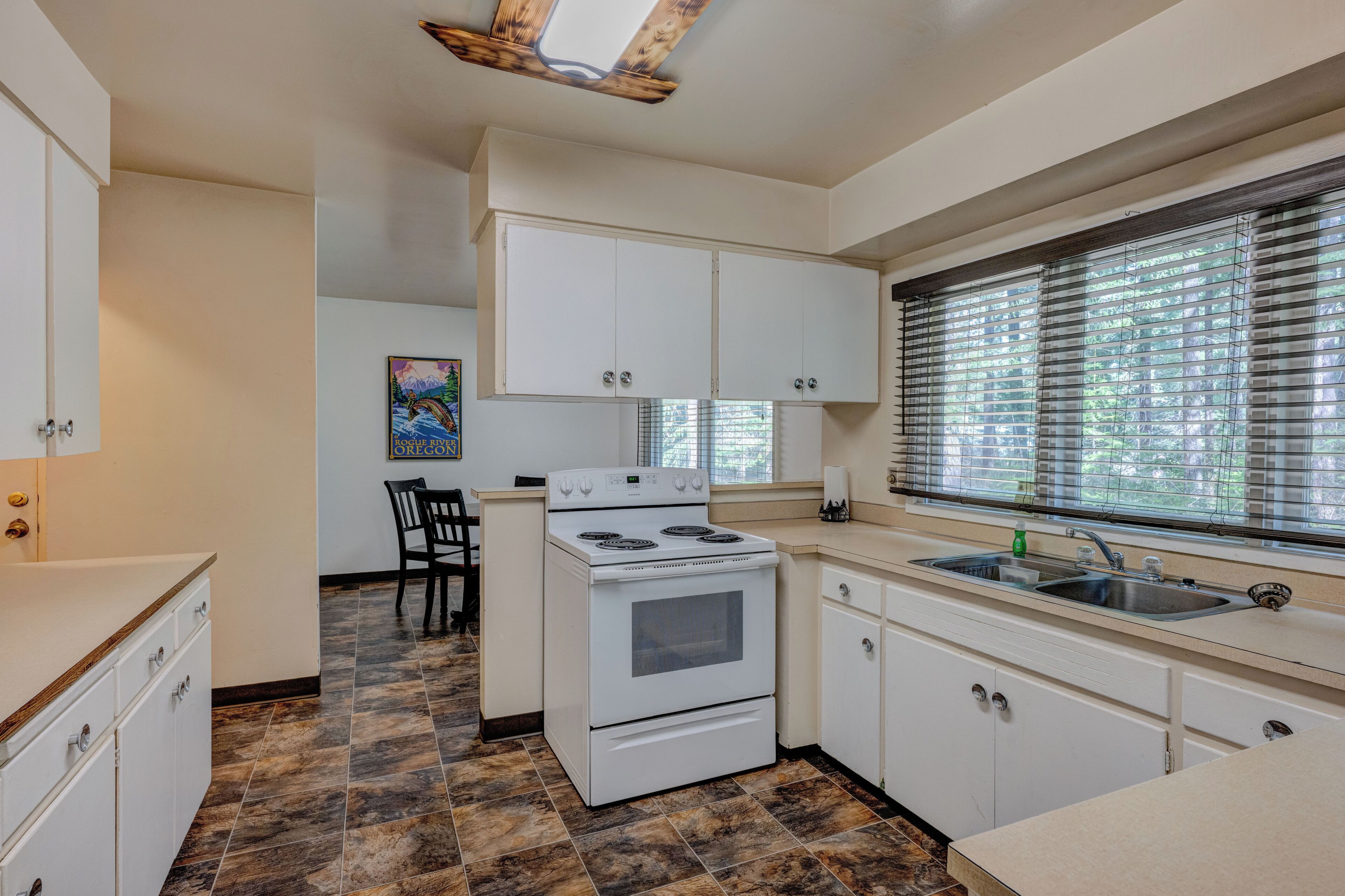 A kitchen with white cabinets, a stove, a sink, and a window with blinds.