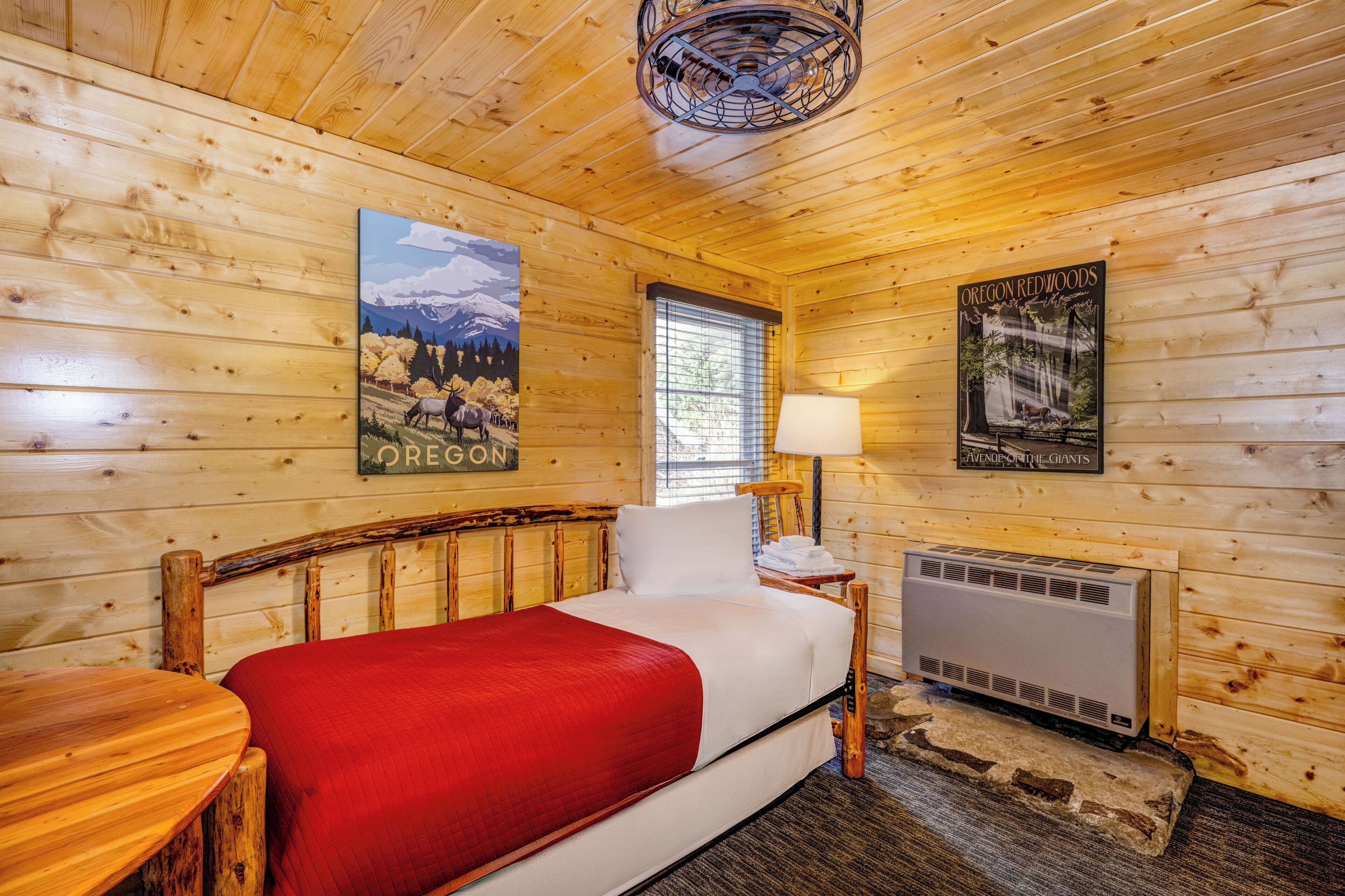 A wooden cabin room with a bed, a window, a lamp, and posters on the walls.