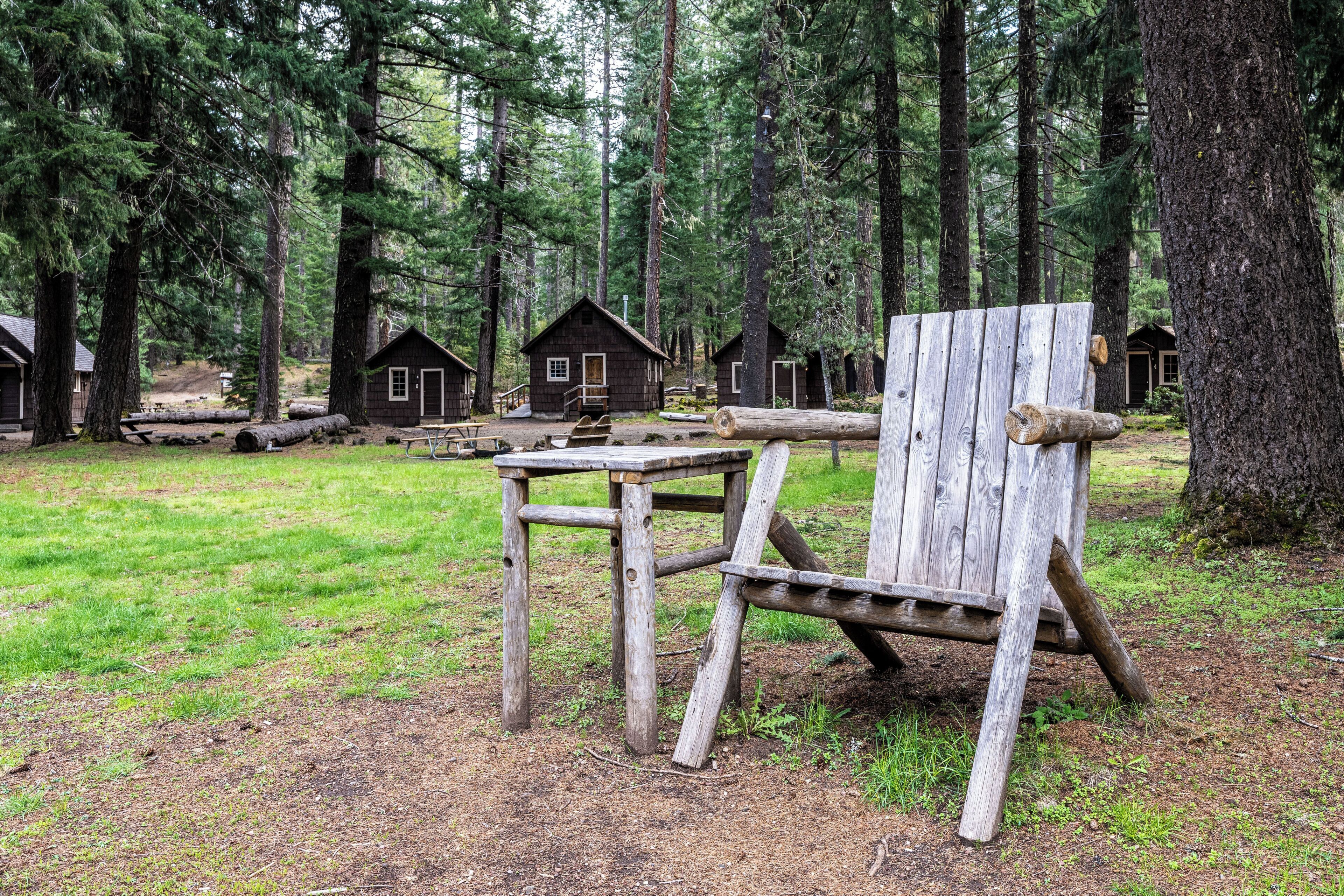 A rustic cabin with a wooden chair and table in a forest setting.