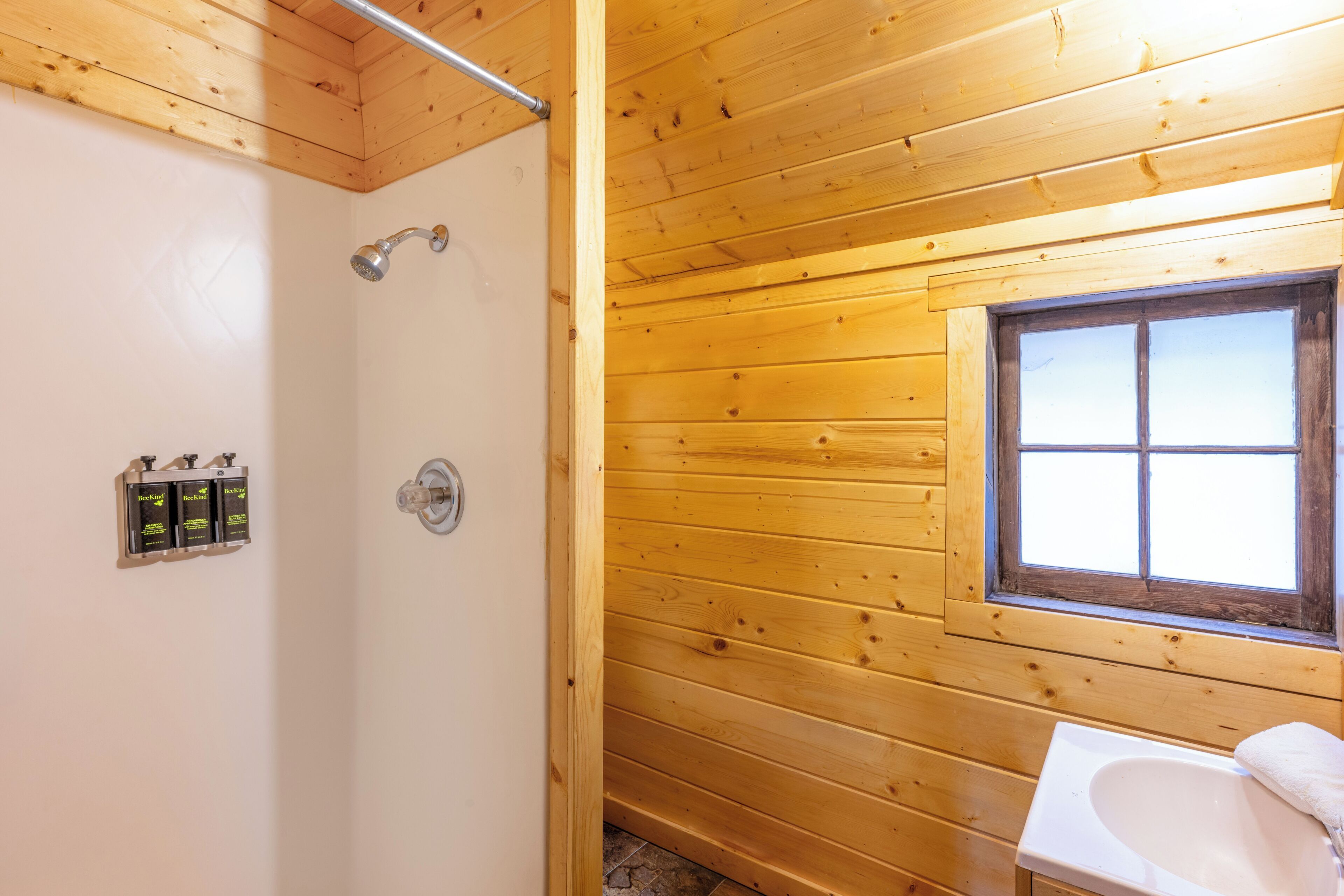 A wooden cabin bathroom with a shower, a window, and a sink.