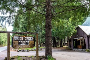 A wooden sign for Union Creek Resort with a contact number, a country store building, and a road in the background.