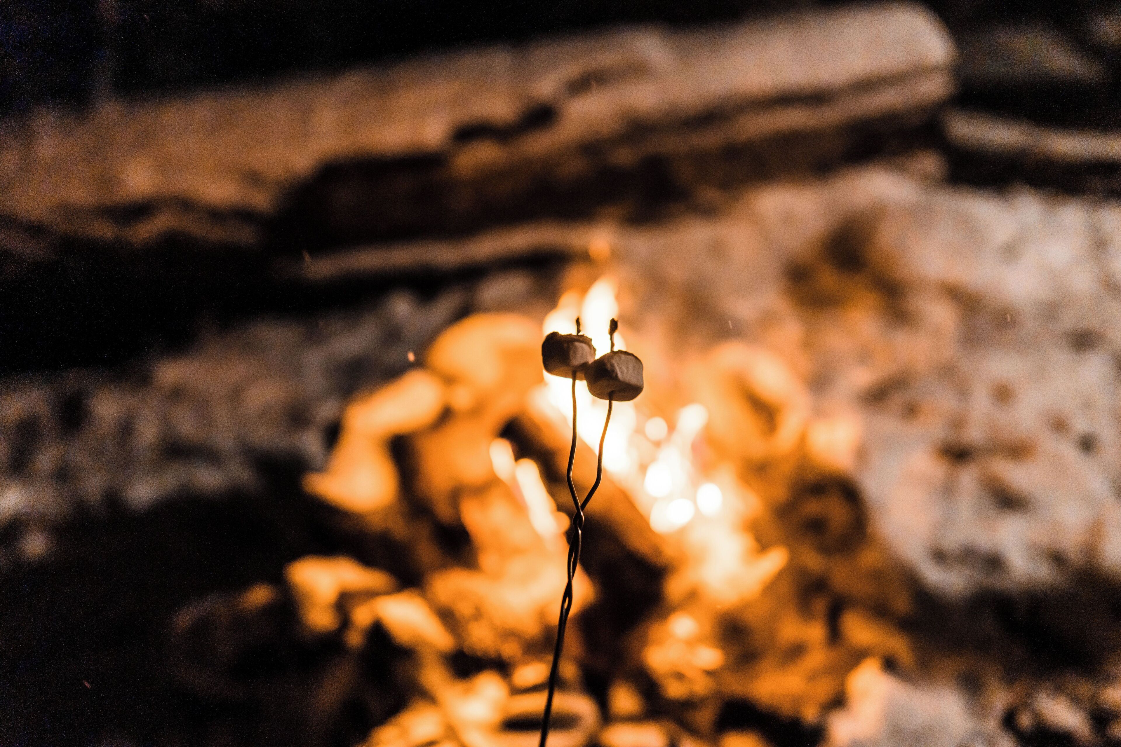 Ein Detailaufnahme einer Kerze mit einer Flamme vor unscharfem Hintergrund aus einer Steinwand und einem Baumstamm.