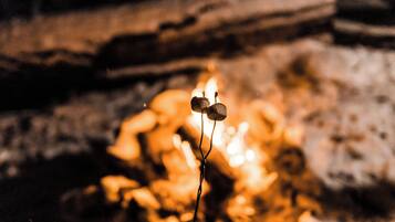 Ein Detailaufnahme einer Kerze mit einer Flamme vor unscharfem Hintergrund aus einer Steinwand und einem Baumstamm.