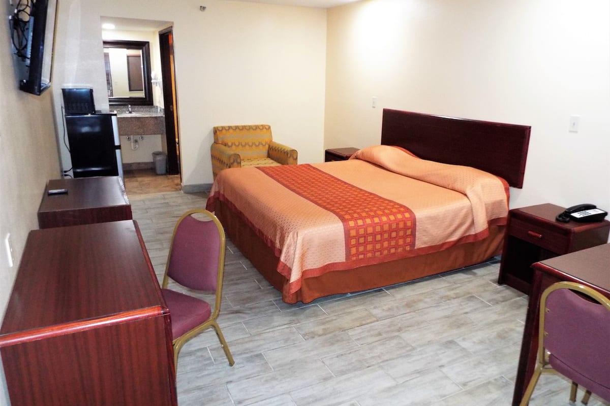 A hotel room with a bed, a desk, a chair, a telephone, and a television.