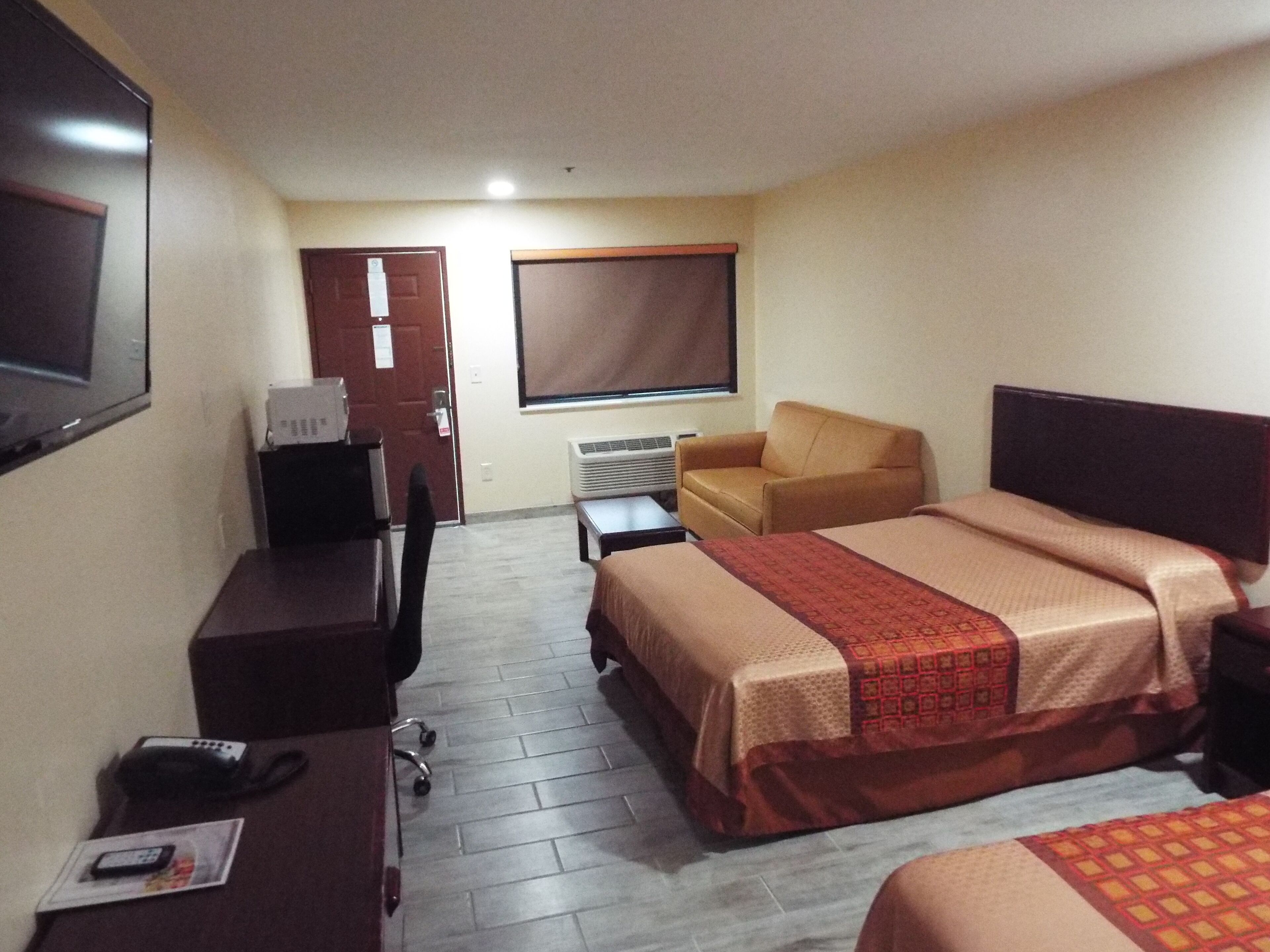 Habitación de hotel con dos camas, un escritorio con computadora, una silla y ventana con persianas.