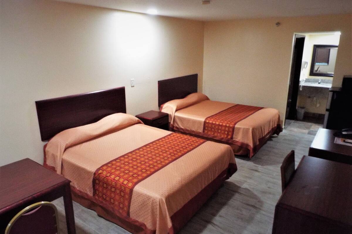 Two single beds with headboards, a wooden nightstand, a desk, and a television.