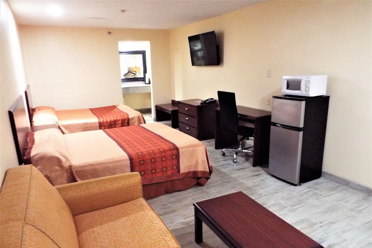 A hotel room with two beds, a desk, a chair, a small table, a television, and a refrigerator.