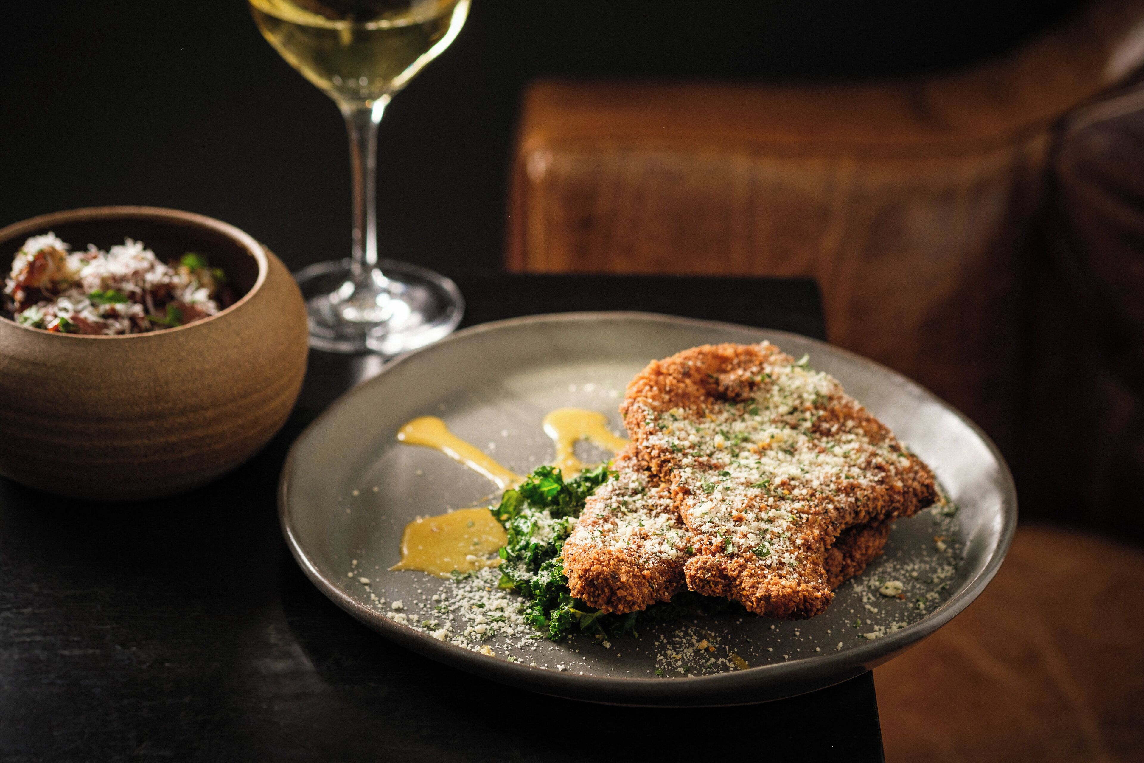 Une assiette de côtelette panée, accompagnée d’une portion de légumes verts et d’un petit bol de sauce.