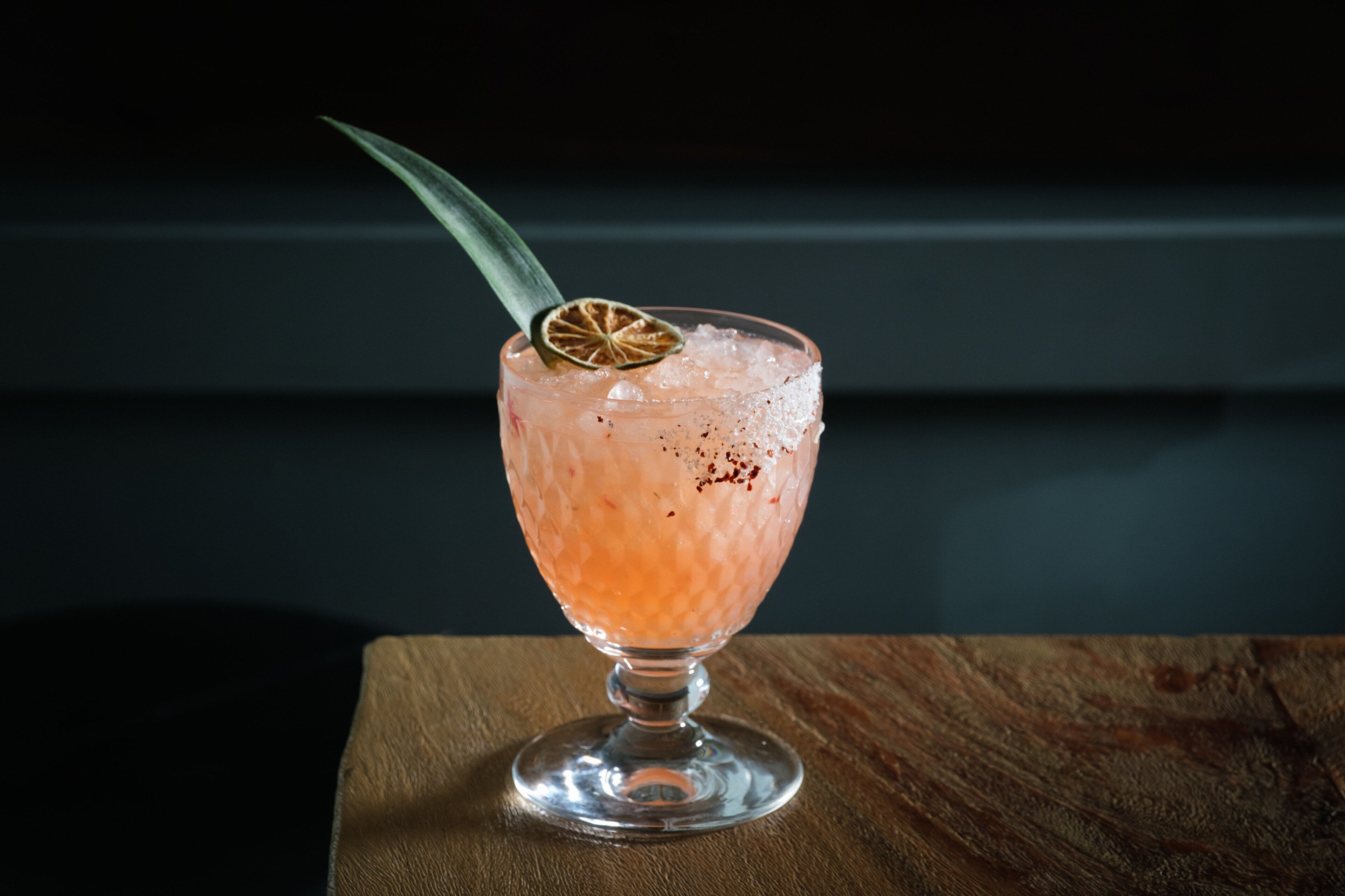 A cocktail in a glass with a stemmed garnish, ice, and a dark background.