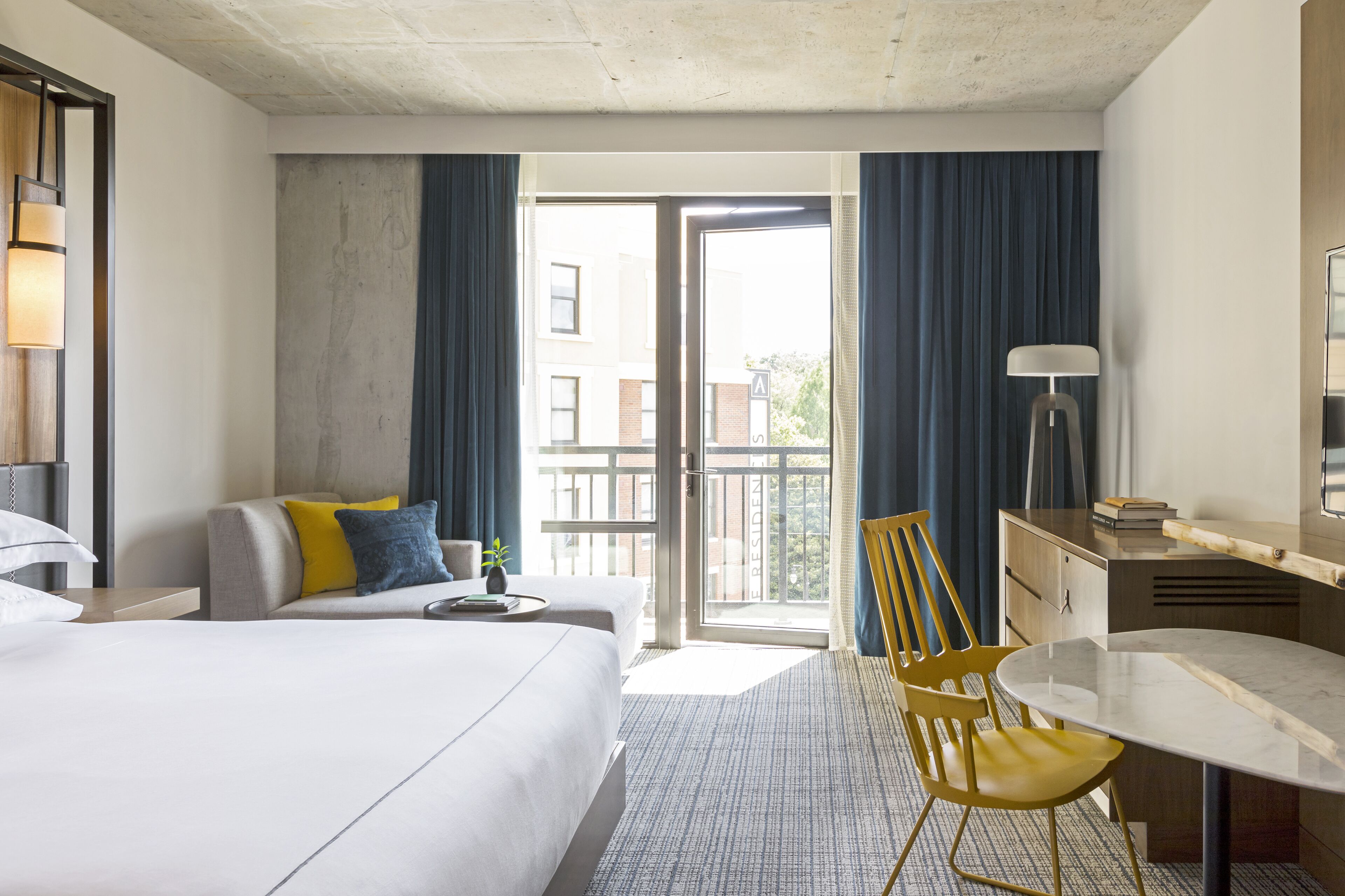 Une chambre d’hôtel équipée d’un lit, d’un bureau, d’une chaise, d’une lampe et offrant une vue sur l’extérieur.