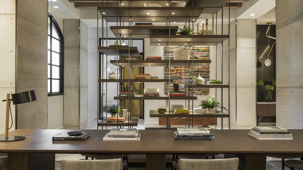 A modern dining area with a long table, two chairs, and a bookshelf filled with books and decorative items. - Kimpton Aertson Hotel by IHG (Nashville)