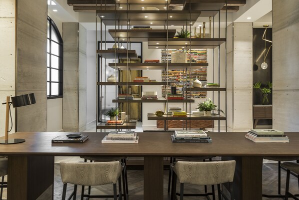 A modern dining area with a long table, two chairs, and a bookshelf filled with books and decorative items. - Kimpton Aertson Hotel by IHG (Nashville)