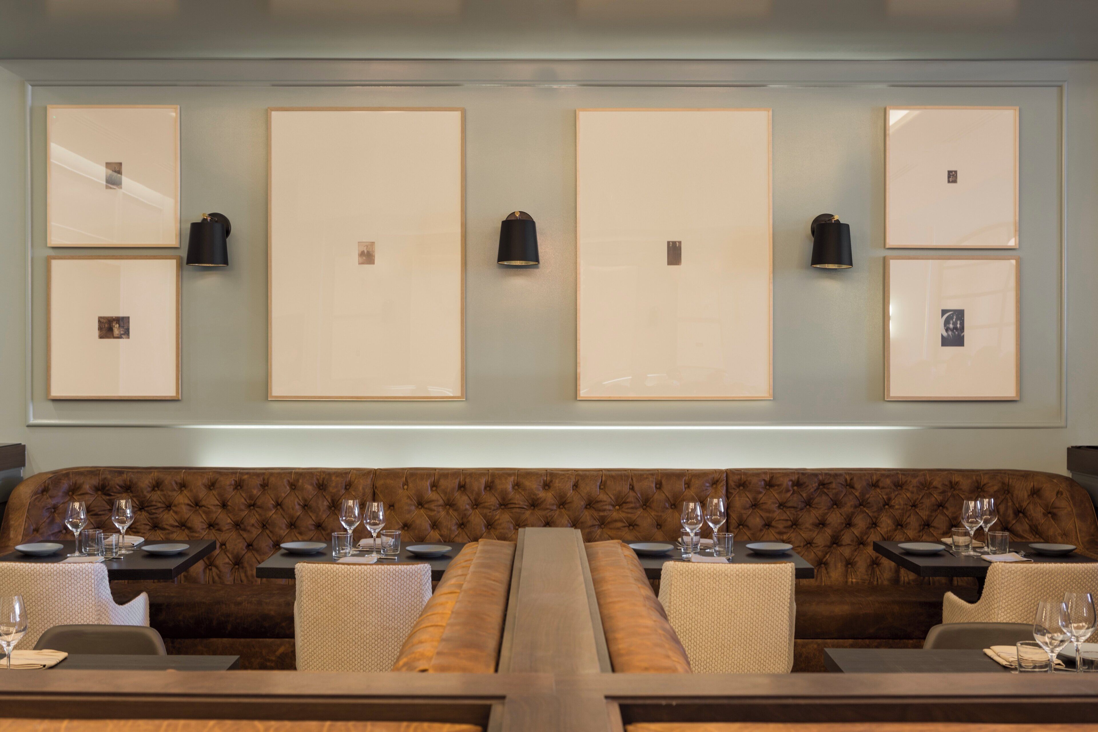 A restaurant with a long wooden table, cushioned booths, and framed pictures on the wall.
