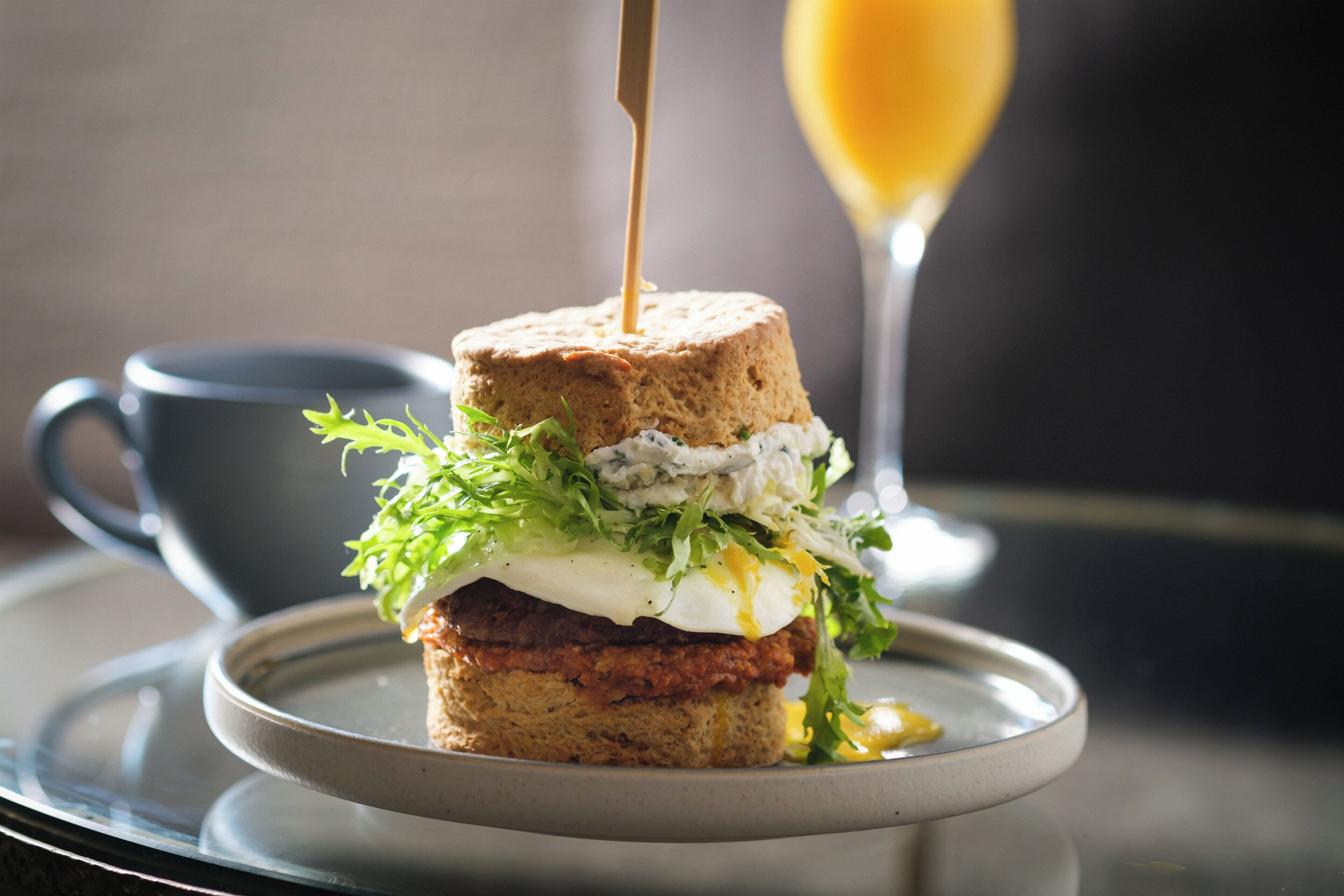 A sandwich on a plate with a glass of orange juice in the background.