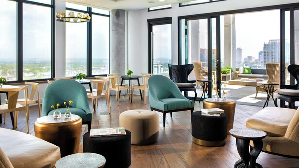 A spacious lounge area with multiple seating options, large windows offering a city view, and a modern interior design. - Kimpton Aertson Hotel by IHG (Nashville)