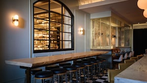 Una zona de bar con una mesa de madera larga, suelo a cuadros blanco y negro y taburetes de bar.